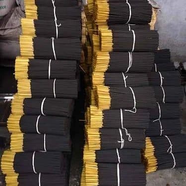 Bundles of raw black agarbatti with yellow stick handles, tied and stacked