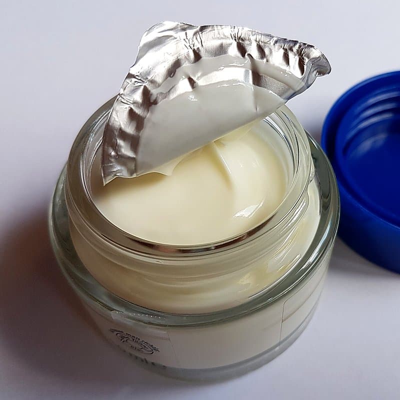 Open glass jar of white face cream with foil liner peeled back