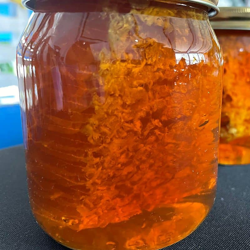 Glass jar of golden honey with a piece of honeycomb inside