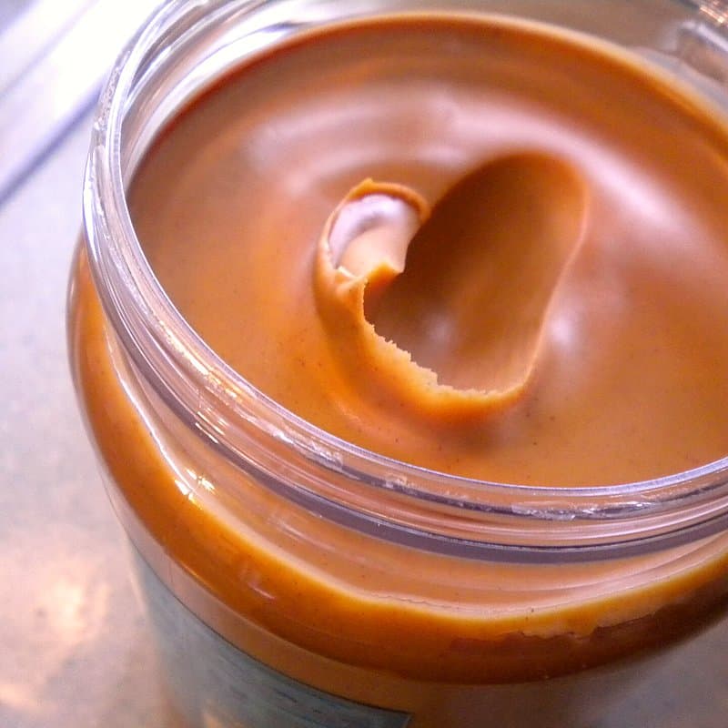 Open plastic jar of smooth peanut butter