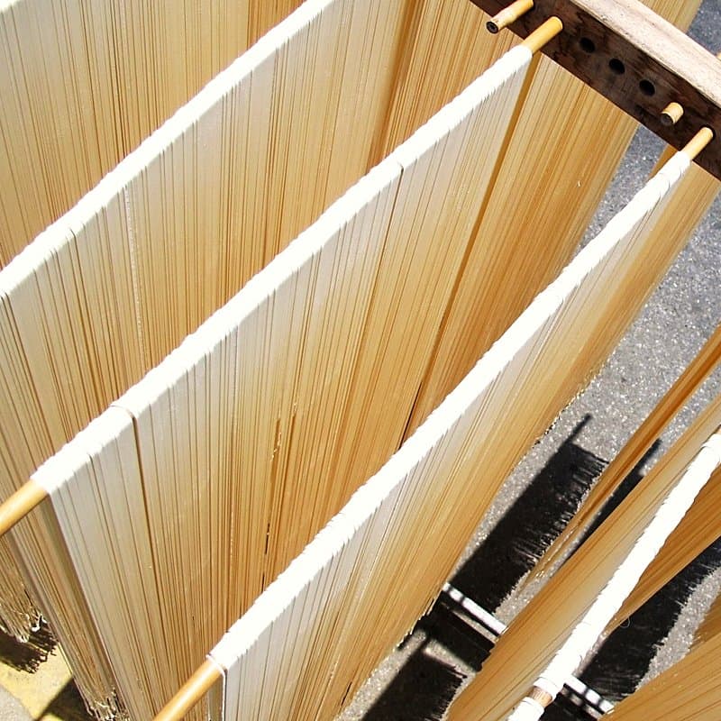 Long wheat noodle strands hanging over wooden poles to dry