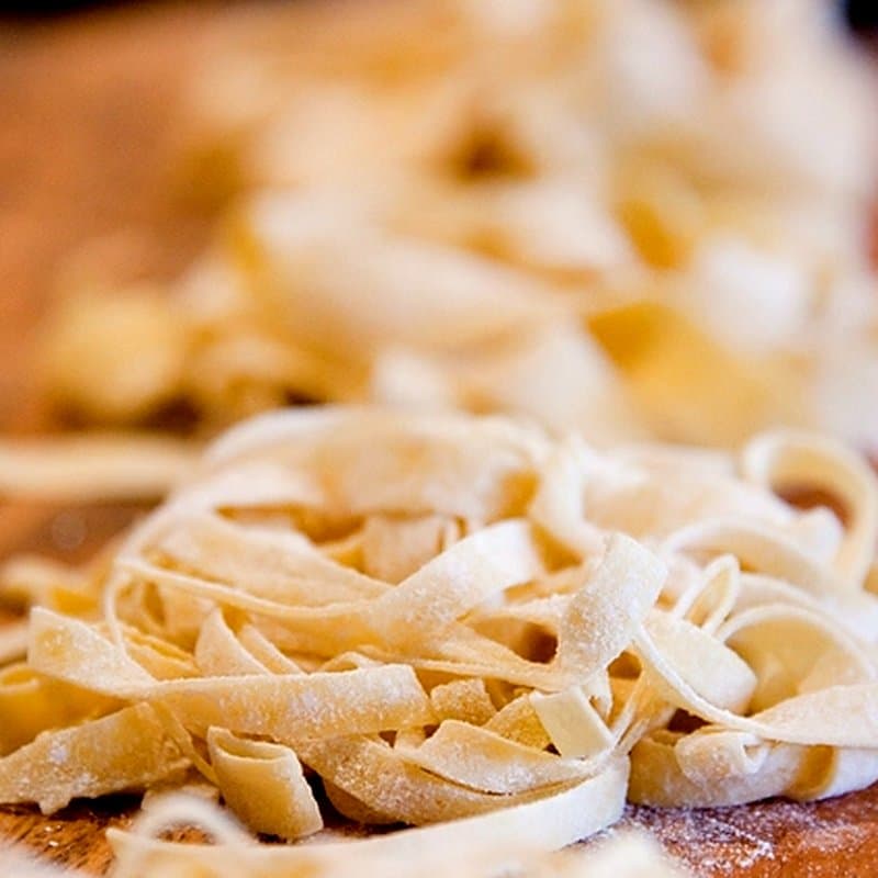Freshly cut flour-dusted noodle strands piled on a wooden board
