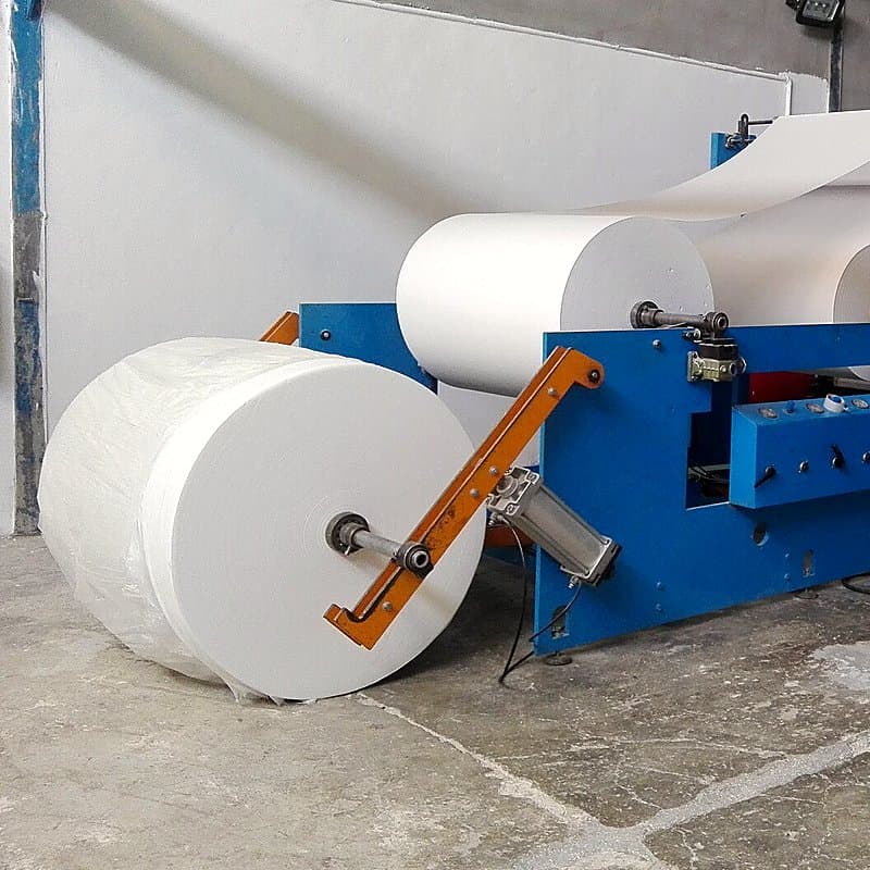 Large white jumbo tissue rolls mounted on a converting machine