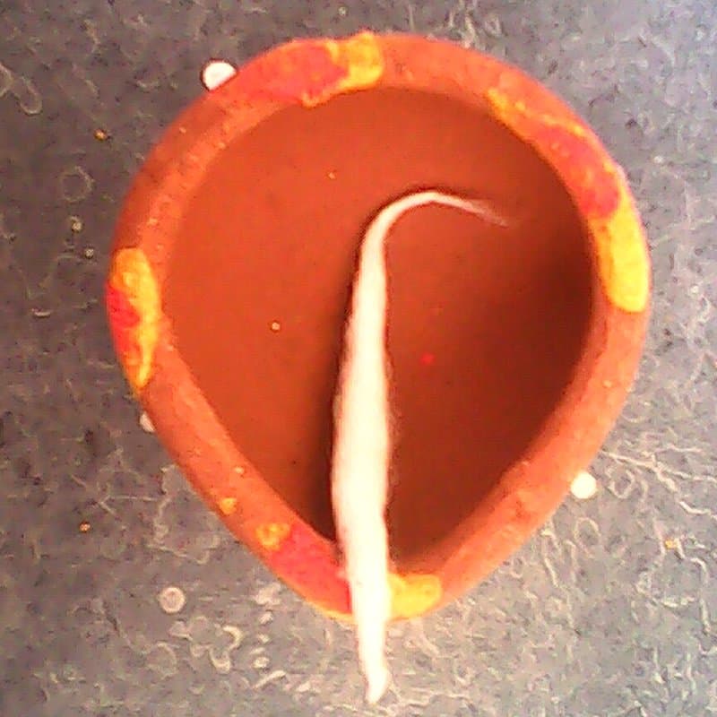 Clay diya with a long white cotton wick laid along it